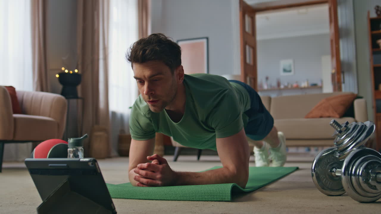 Sportsman watching workout tutorial video by tablet training at home close up.