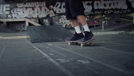 hombre deportivo haciendo ejercicio en la tabla de skate en el skatepark con pared de graffiti.