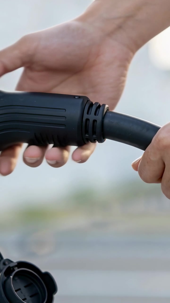 Vertical video: Gripping charger plug, driver hands aligning and seating it into inlet to charge