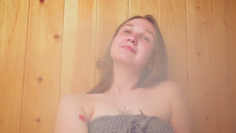 woman wrapped in towel, relaxing in sauna and having a good time, eyes closed, enjoying a soothing moment, she sits calmly on the wooden bench in a peaceful, serene environment