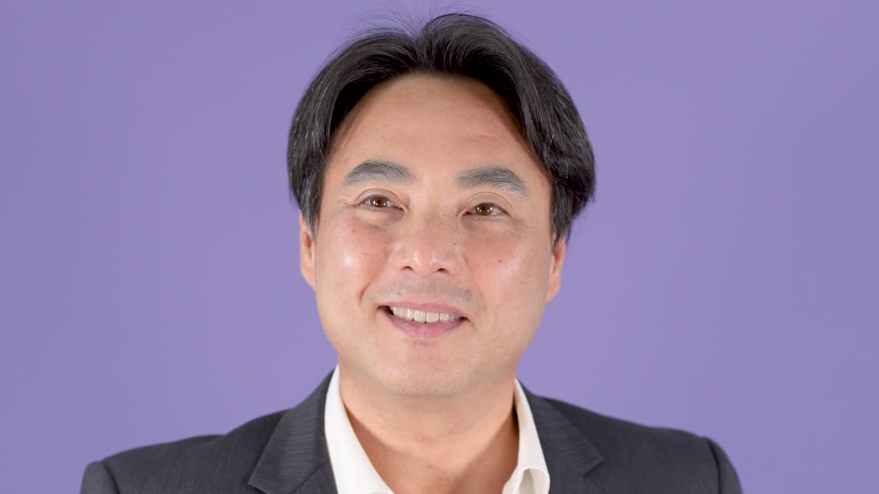 自信に満ちた中年ビジネスマンが、紫色の背景のクローズアップスタジオポートレートで笑顔でまばたきをしています。