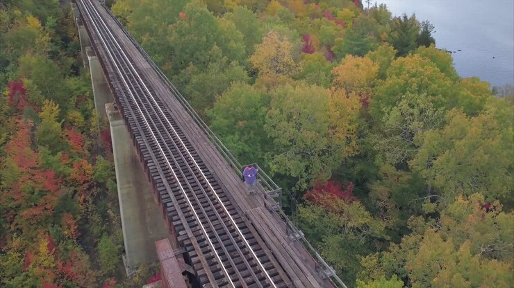 Lone traveler standing on train tracks with autumn trees and lake Onawa in the distance