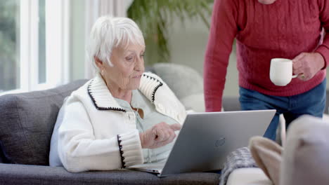una feliz pareja caucásica sentada en el sofá usando una computadora portátil en casa, en cámara lenta