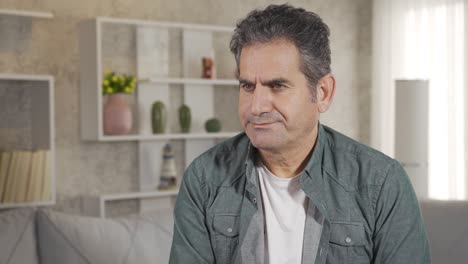 Close-up-shot-of-thoughtful-mature-adult-man-with-gray-hair-sitting-alone-at-home-thinking-about-life-alone