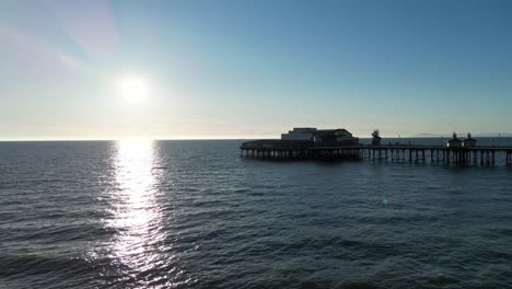 Aerial-drone-flight-heading-out-to-sea-heading-over-a-pier-at-Blackpool-Beach-with-the-sun-shining-down-over-the-ocean