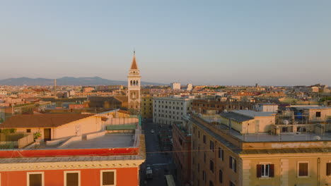 Aerial-footage-of-old-apartment-buildings-in-urban-borough-at-golden-hour.-Tower-with-decorations-protruding-above-town-development.-Rome,-Italy