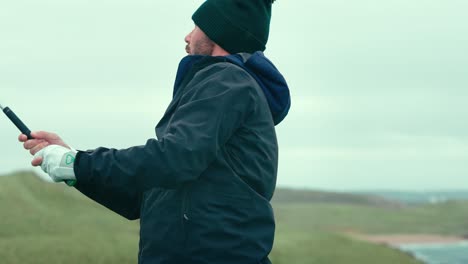 male golfer hitting driver off golf course tee box on cold ireland day in slow motion