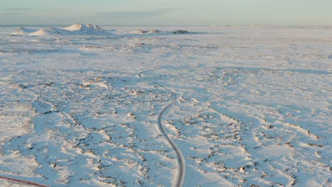 Bláa-lónið-remote-road-through-volcanic-landscape-during-winter,-aerial