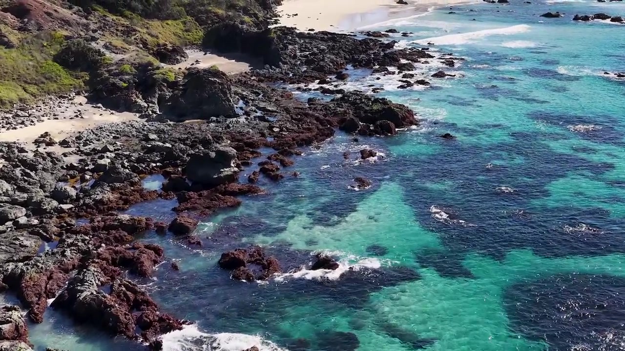 Avustralya, Port Macquarie'de berrak turkuaz su ve koyu renkli kayaların yüksek açılı drone çekimi