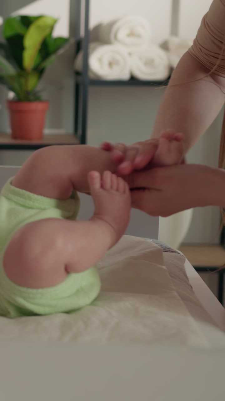 Un progenitor masajea suavemente la pierna y el pie de un bebé en un cambiador, con iluminación suave y plantas.