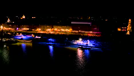 Garonne-river-shore-at-night-in-Bordeaux-France-during-Wine-Fair-with-large-crowds-celebrating,-Aerial-pan-right-shot