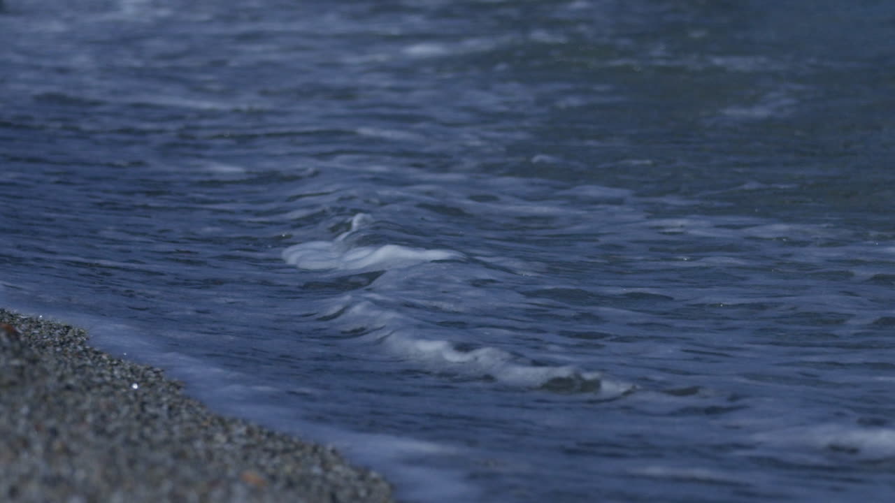 Small waves roll in to the shore on the shore line of a pebble beach in Marbella, Spain