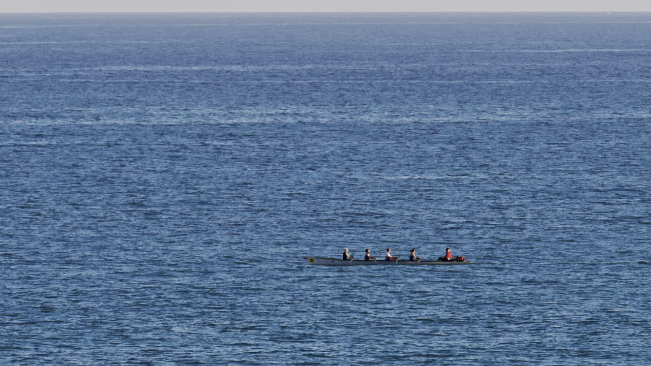 Distant view of a rowing team of four people practicing on calm water, with a coxswain seated at the front