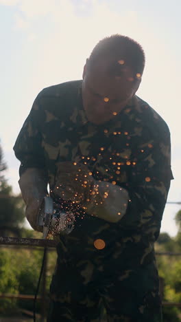mature builder in camouflage uniform cuts metal plank with circular saw in yard at bright sunlight