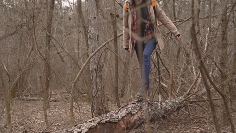 uma jovem irreconhecível se equilibra sobre um tronco de árvore caído no meio da floresta