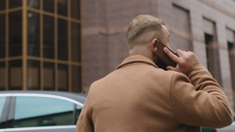 rear view of caucasian good looking businessman walking on the street and talking on the phone