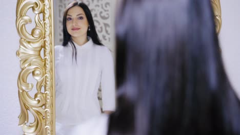 a satisfied brunette in a white dress looks in the mirror at the result of the work of the master after the procedure of permanent lip makeup. close-up.