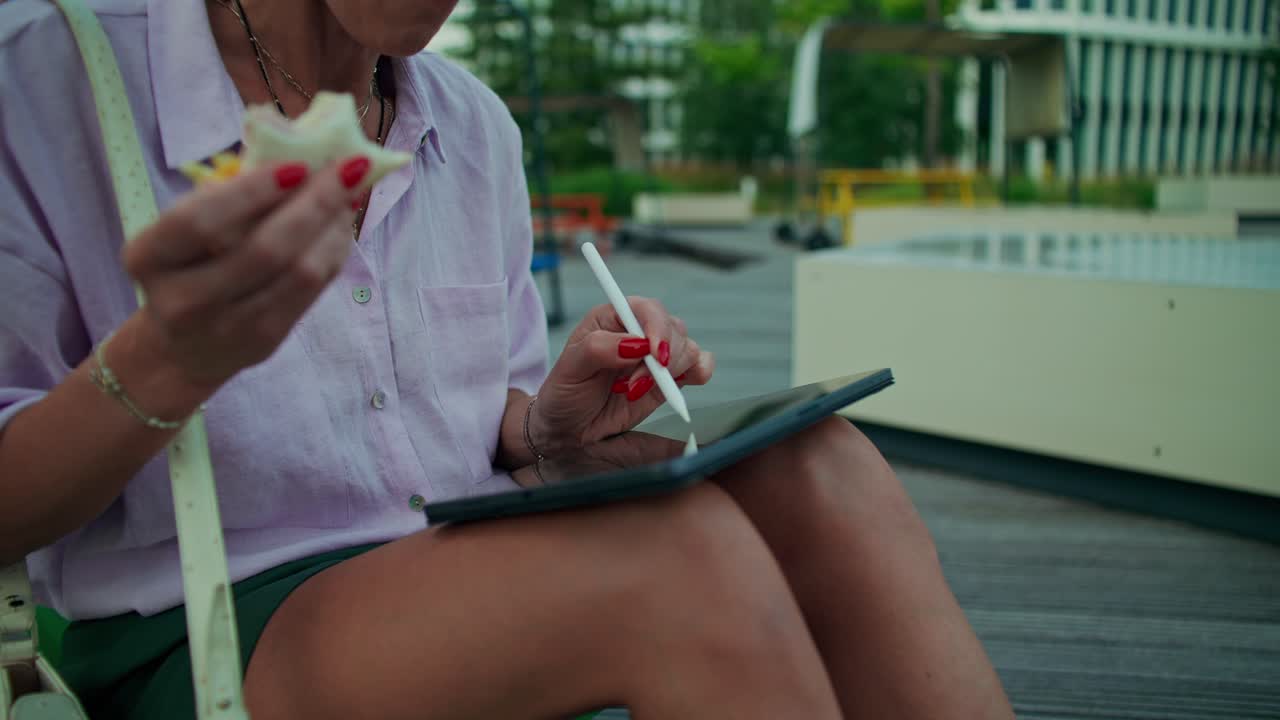 Woman using tablet and eating lunch outdoors