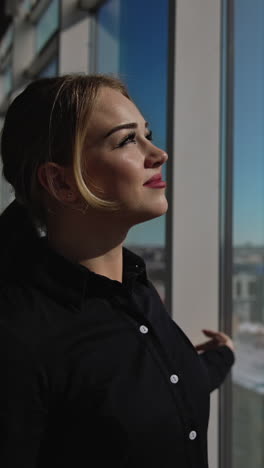 attractive female enjoying the sunrays coming through the big panoramic window. great look at the city from the office center. close up with gradual distancing. vertical video