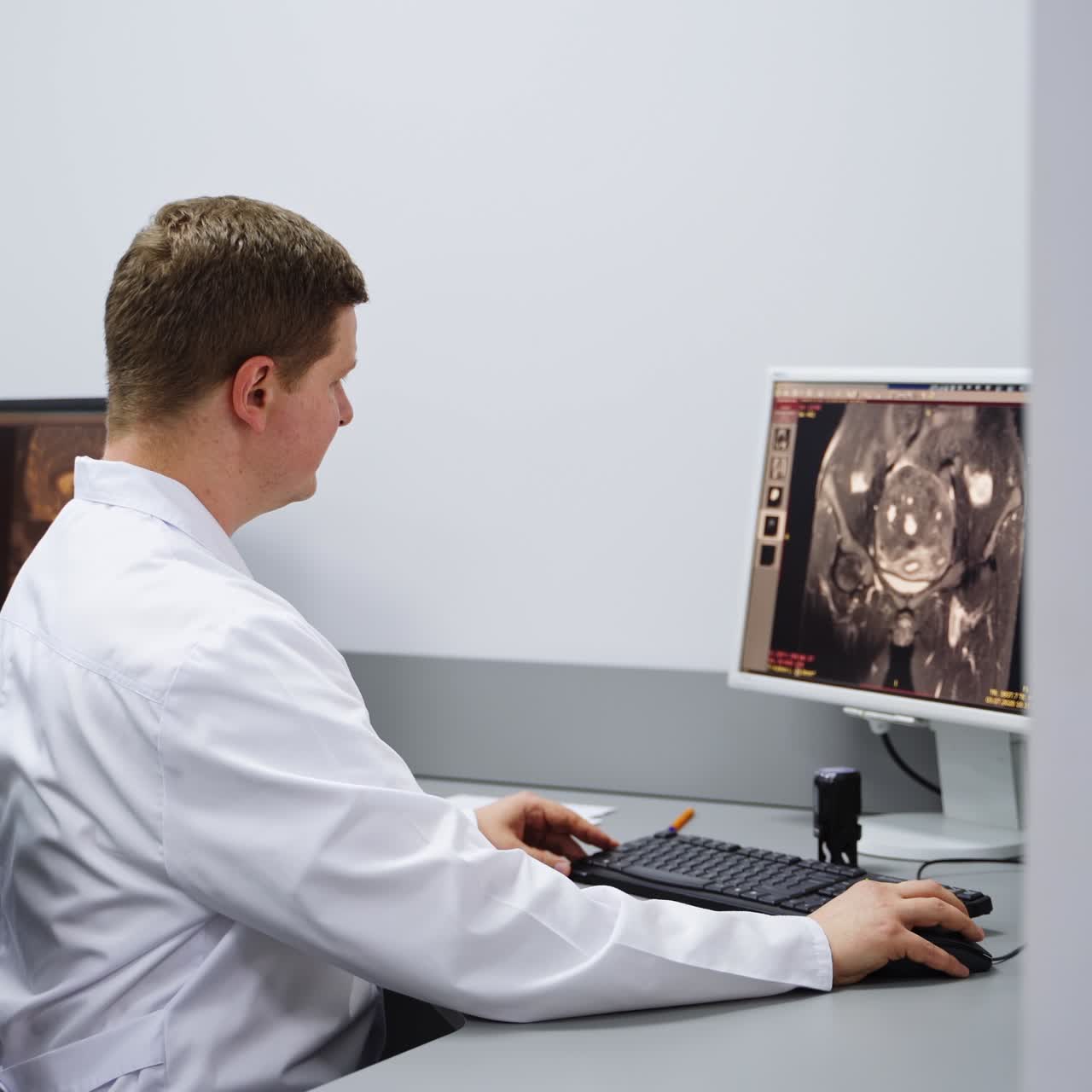 Male lab technician wearing white robe sitting at the table. Professional checking up different scans on the computer screen. MRI shots analysis