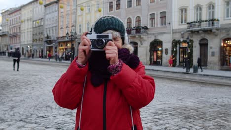 senior woman tourist taking pictures with photo camera, using retro device in winter city center