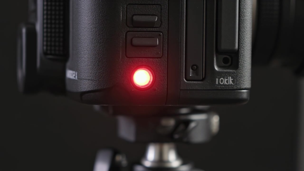 Showing camera side panel as cam powering and red LED cycling against dark studio backdrop, tripod