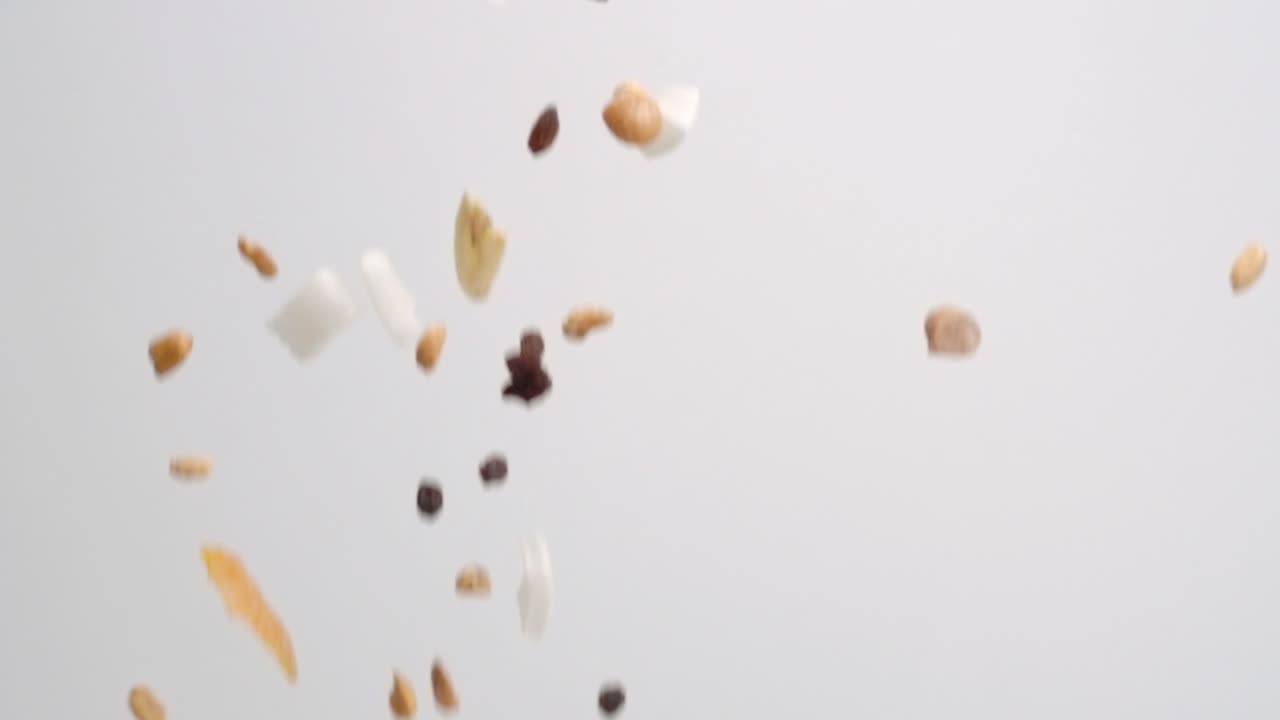 Sweet and salty tropical trail mix with dried fruit slices, coconut, raisins and nuts raining down on white backdrop in slow motion