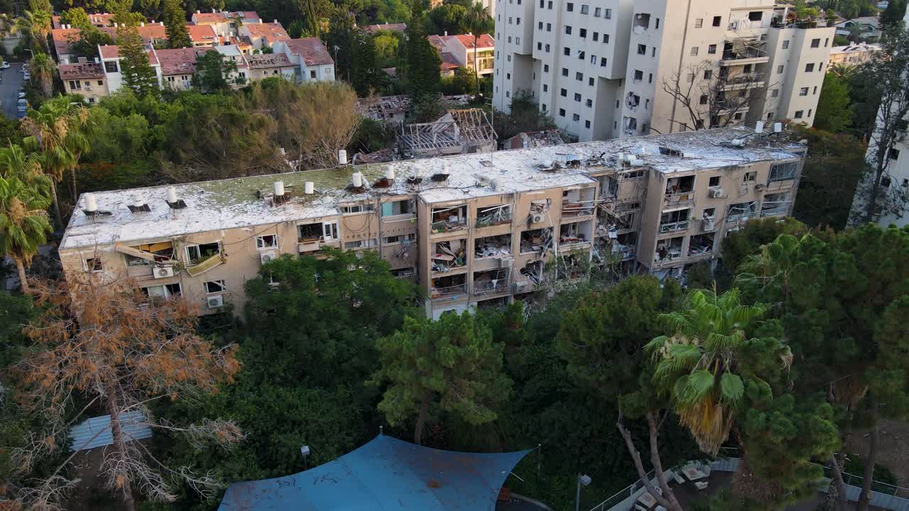 High lateral drone shot shows a damaged residential block in North Tel Aviv, surrounded by trees and nearby buildings.