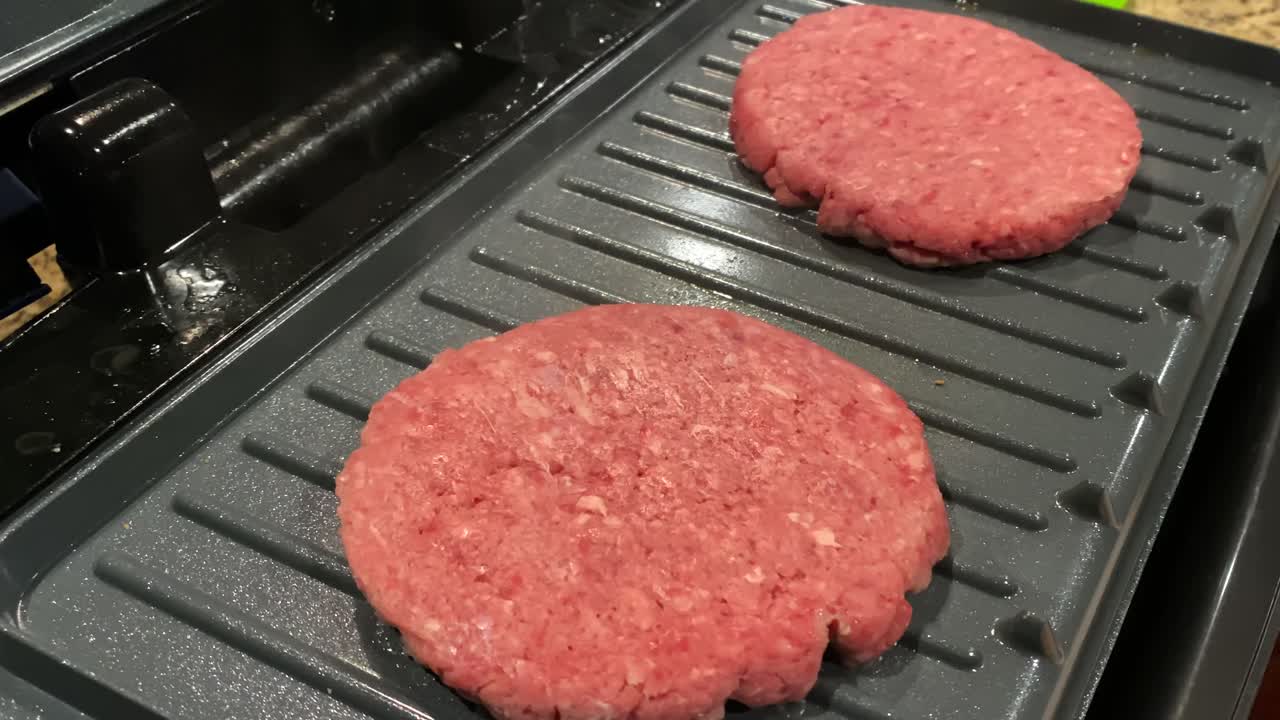 Hamburger di carne cruda che cuociono sulla griglia a casa, primo piano.