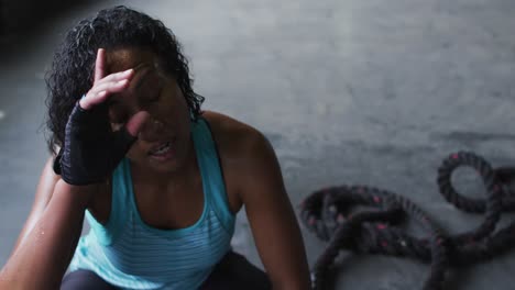 mujer afroamericana descansando después de luchar con cuerdas en un edificio urbano vacío