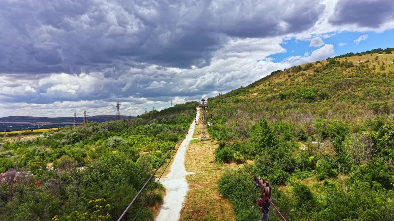 Sendero a través de colinas verdes bajo un cielo nublado con tendido eléctrico y una vista lejana de montañas