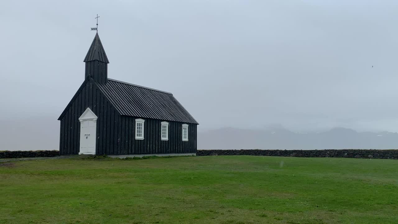 The black church Budakirkja in the south western part of Iceland on the Snæfellsnes peninsula, standing on green grass on a rainy and foggy day