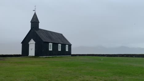 the black church budakirkja in the south western part of iceland on the snæfellsnes peninsula, standing on green grass on a rainy and foggy day