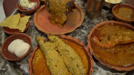 vista di profilo di pesci, rasgullas, gamberetti, papad, chutney e alcuni altri piatti forniti su piatti di argilla e acqua su vetro di bronzo