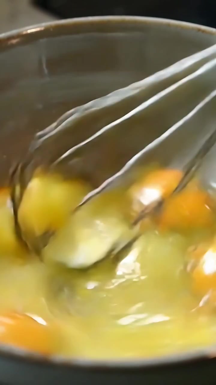 Vídeo vertical: Batedor de metal entrando no quadro, quebrando gemas e misturando quatro ovos em uma tigela perto do fogão.