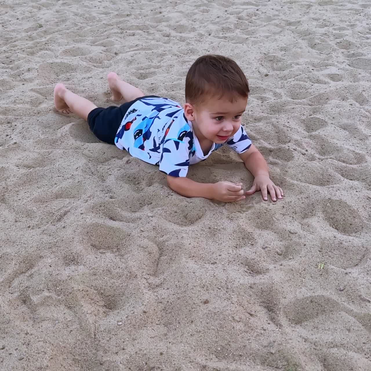 Grazioso e adorabile bambino che gattona sulla sabbia bianca all'aperto. Il bambino felice si sdraia sulla sabbia per riposare.
