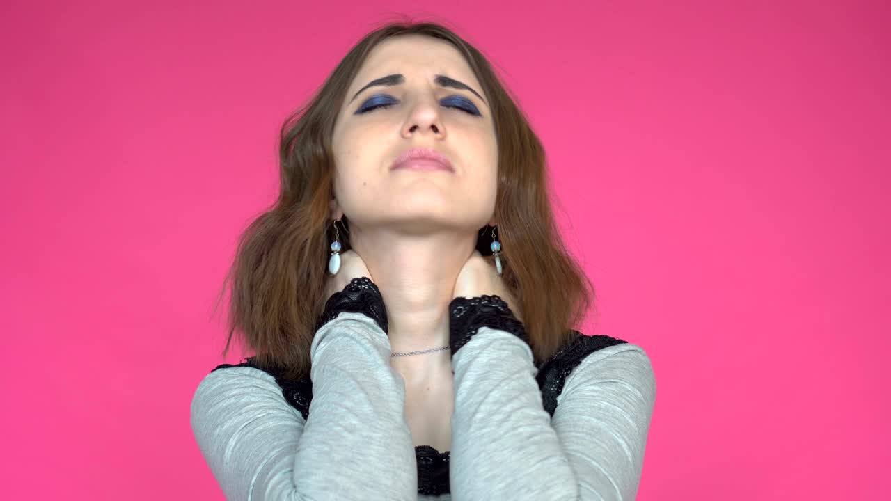 Young woman having pain in neck over pink background.