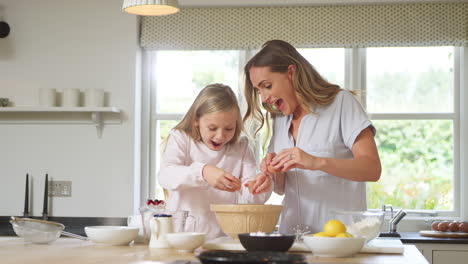 mother and daughter wearing pyjamas baking and making pancakes in kitchen at home together