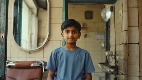 portrait of a young boy standing in a vintage barbershop, waiting for a haircut, with an old barber chair and a mirror in the background, exuding a nostalgic atmosphere