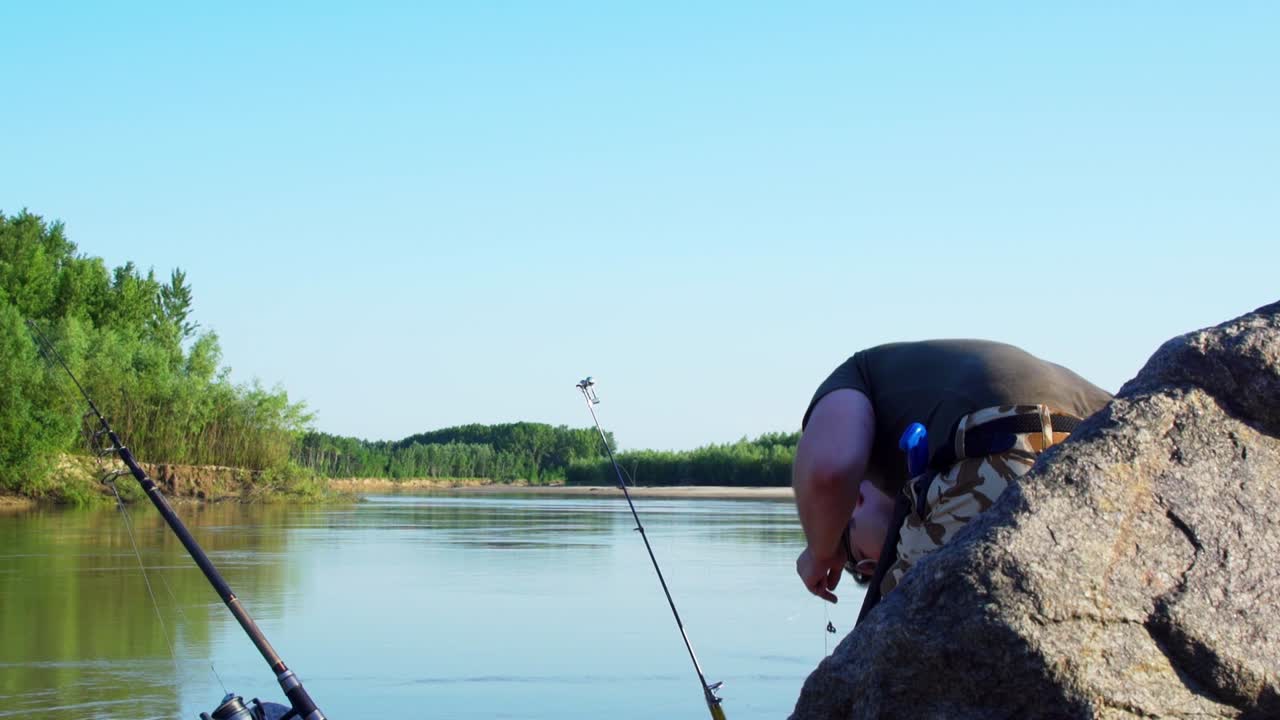 Man With Two Fishing Rods Preparing His Fishing Lures Standing On The Banks Of Siret River In Galati Country, Romania