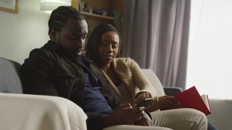couple at home sitting on sofa in lounge having argument over what man is looking at on mobile phone