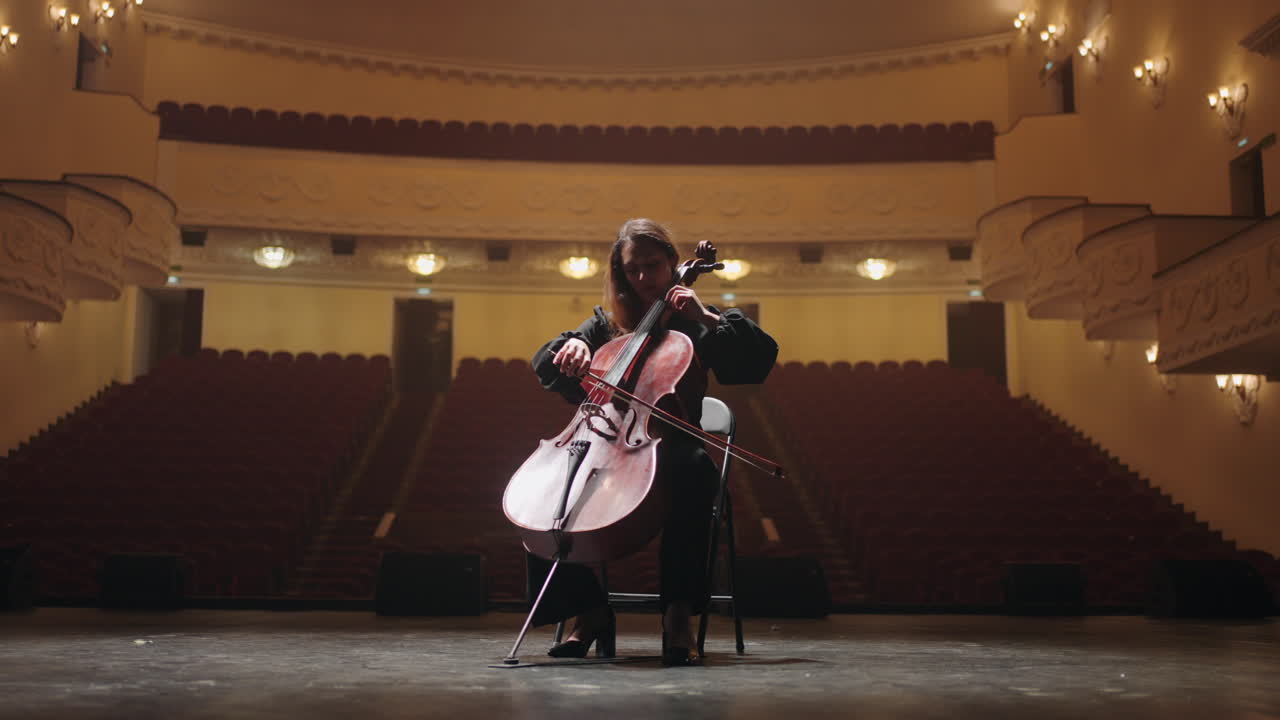 una mujer solitaria está tocando el violonchelo en la sala de música vacía de la ópera. una violonchelista está ensayando.