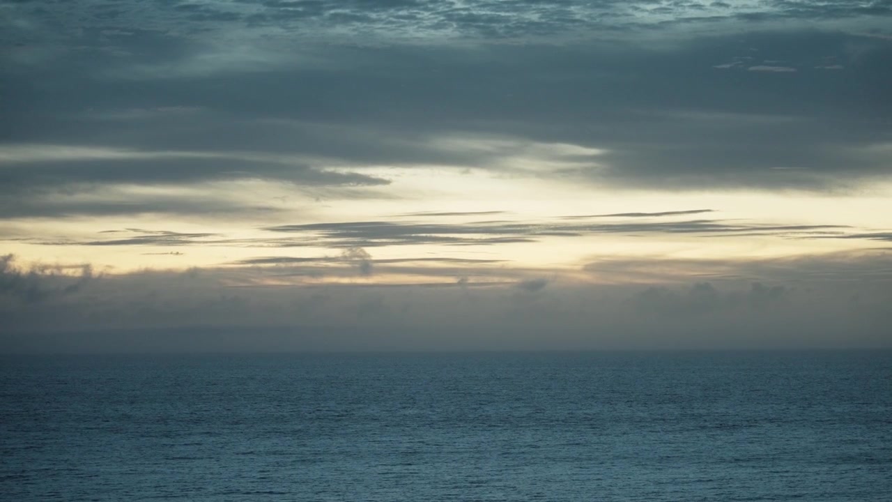Static shot of ocean horizon under cloudy sky at sunset light