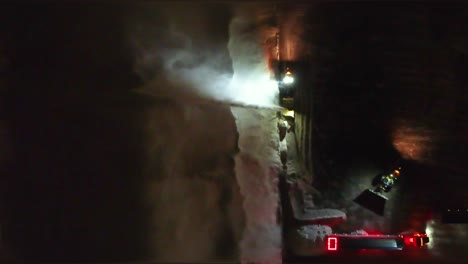 Top-view-of-a-snow-blower-truck-clearing-snow-to-the-side-of-the-road-at-night