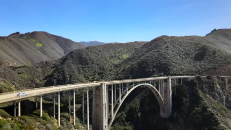 bixby bridge in big sur, aerial rising view, cars driving on bridge, mountains on a clear day