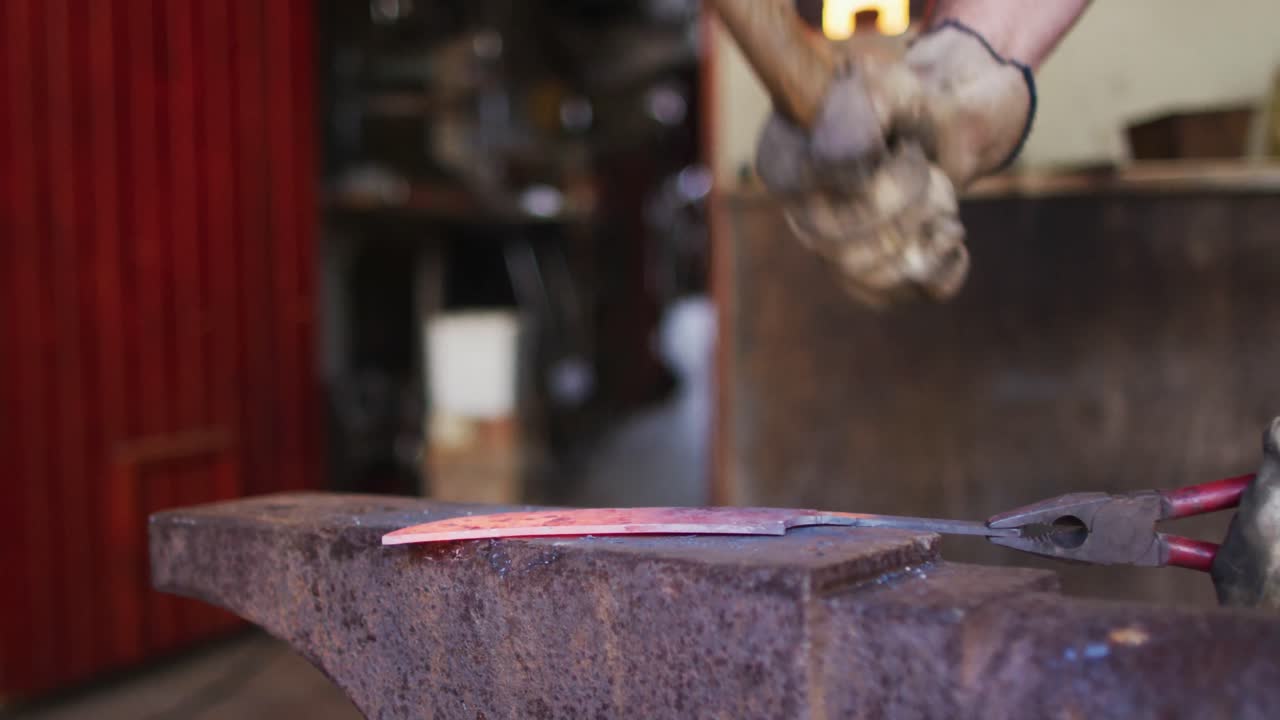manos cercanas de un hombre caucásico fabricante de cuchillos en un taller sosteniendo un martillo y haciendo un cuchillo