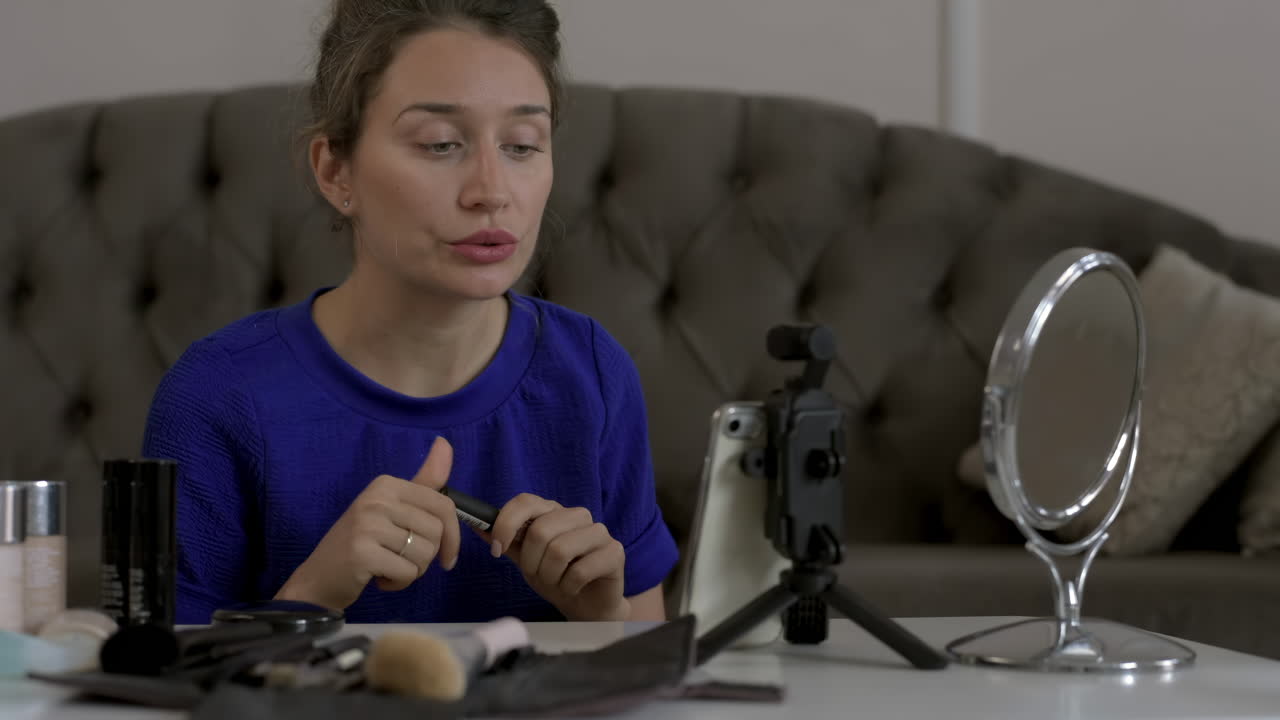 Woman in a blue T-shirt filming herself while doing a make-up tutorial at home