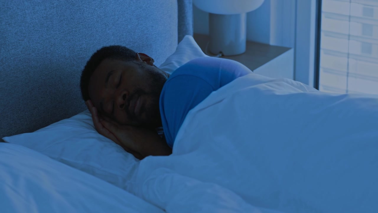 Ung afroamerikansk mand sover fredeligt i sengen om natten