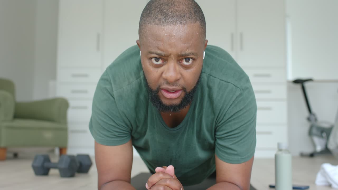 African American man starting workout holding forearm plank on dark mat, building core strength
