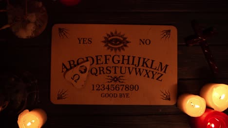 close up video of a wooden ouija board on a table surrounded by candles and a cross in a muffed - close up video of a wooden ouija board on a table. wax candles and a cross around. the planchette is slowly moving across the board, spelling out words and numbers. creative mystical content